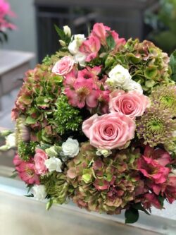 Ramo de alstroemerias, rosas, hortensias y otras flores en tonos rosados y verdes.