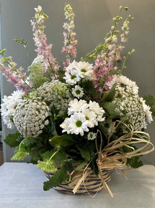 Centro de flores en cesta de mimbre con delphinium, margaritas, amimajus, con verdes variados.